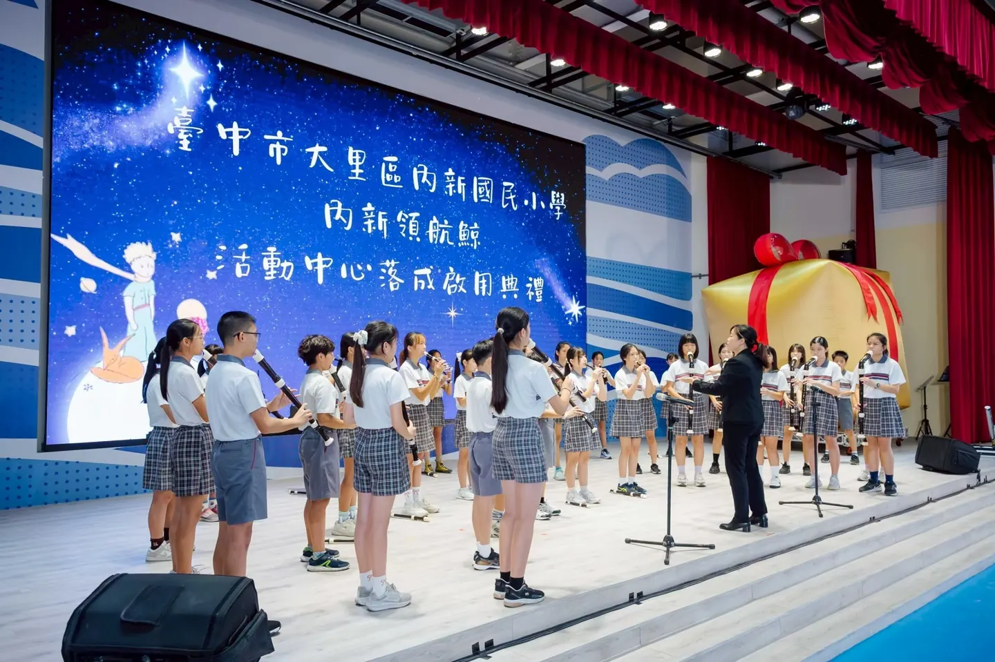 學生在舞臺上演奏，老師在一旁指揮
